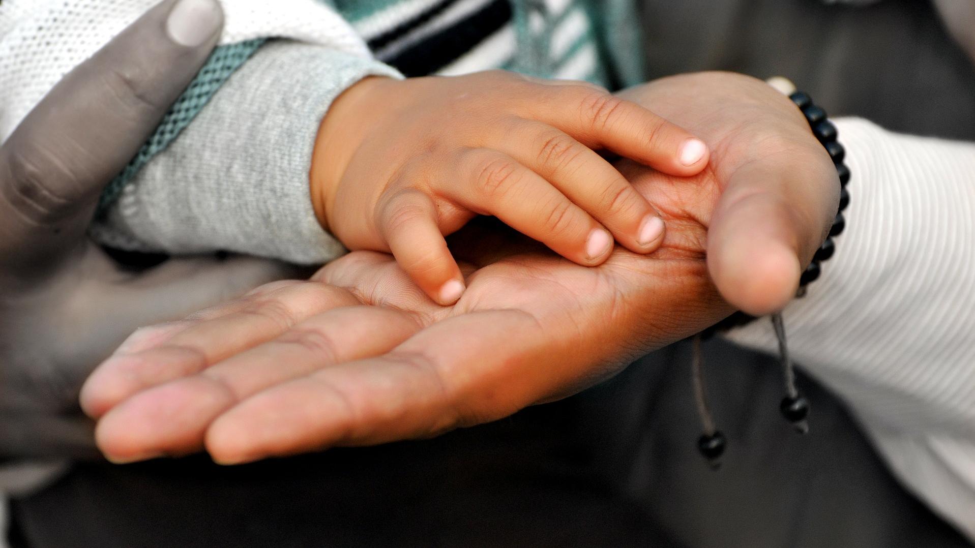 Stimmungsbild zum Beitrag: Eine Babyhand liegt auf der Hand eines Erwachsenen.