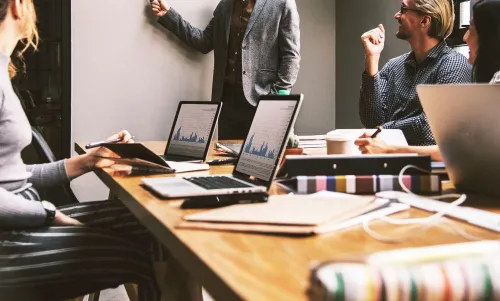 Stimmungsbild zum Beitrag: Es werden vier Arbeitnehmende um einen Tisch verteilt mit Laptops abgebildet.
