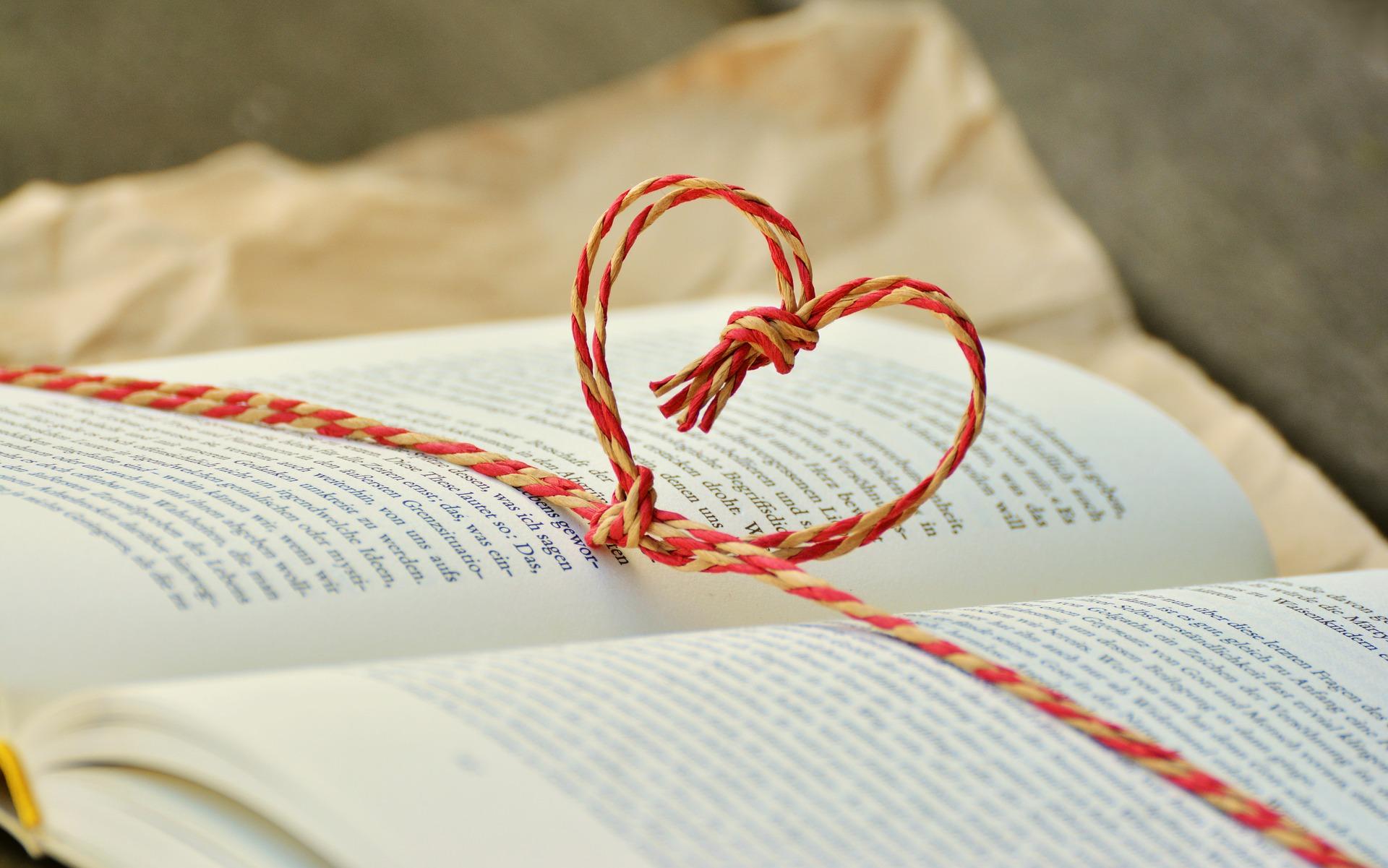 Stimmungsbild zum Beitrag: Ein aufgeschlagenes Buch, um das ein Band mit Herzform geknüpft ist, wird abgebildet.