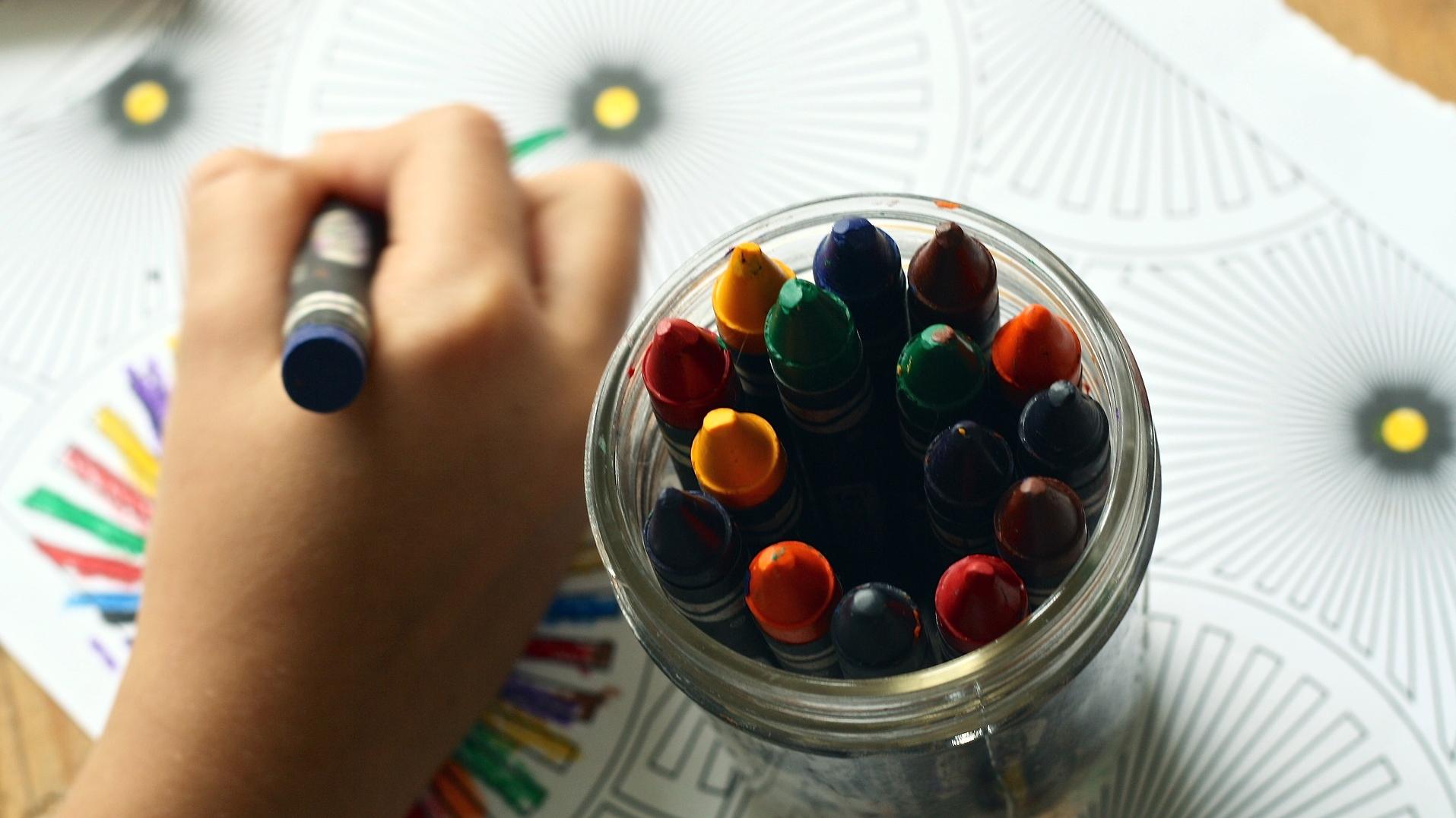 Stimmungsbild zum Beitrag: Ein Kind malt mit Wachsmalstiften ein Malbuch aus.