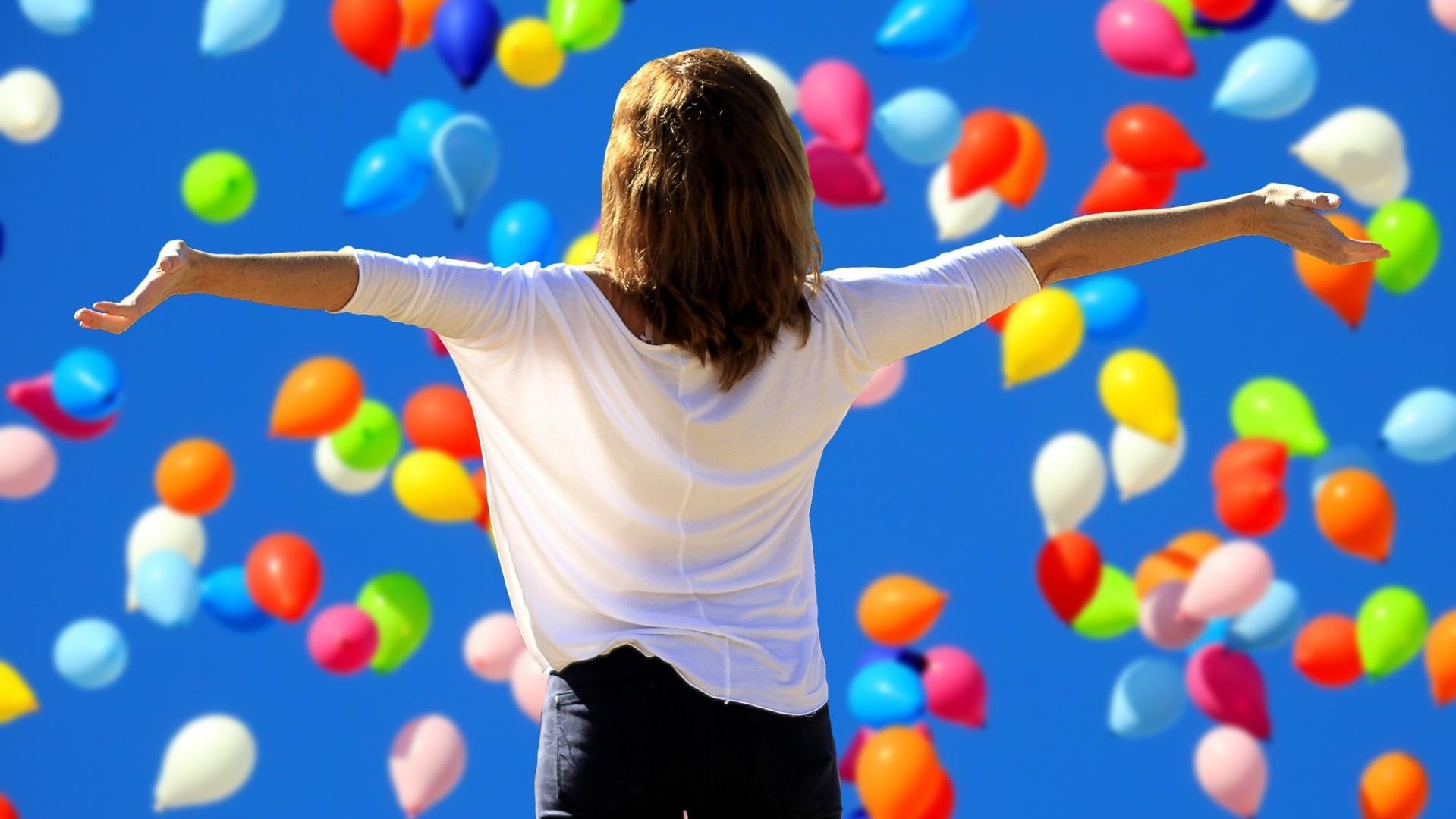 Frau steht mit ausgebreiteten Armen vor einem Horizont, der gefüllt mit Luftballons ist.