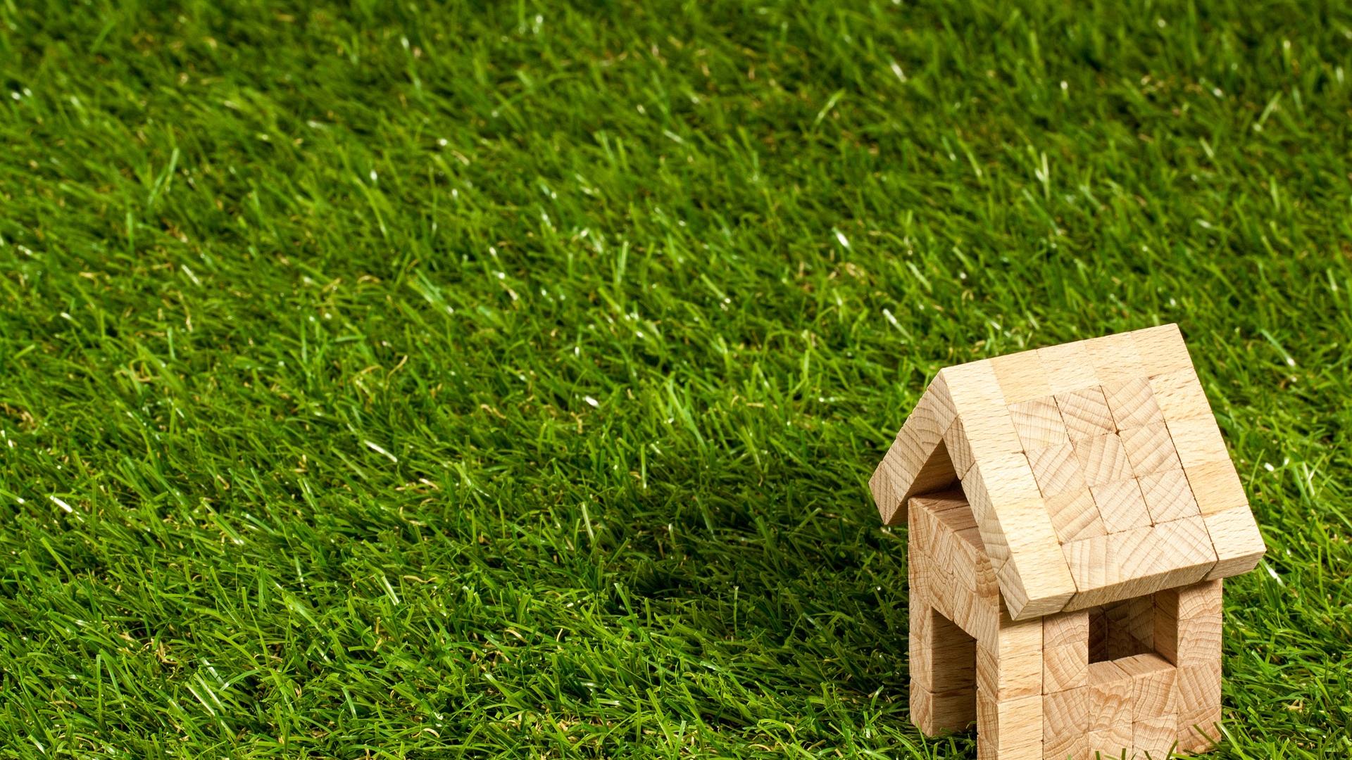 Stimmungsbild zum Beitrag: Es wird ein Modelhaus aus Holz auf Rasen abgebildet.