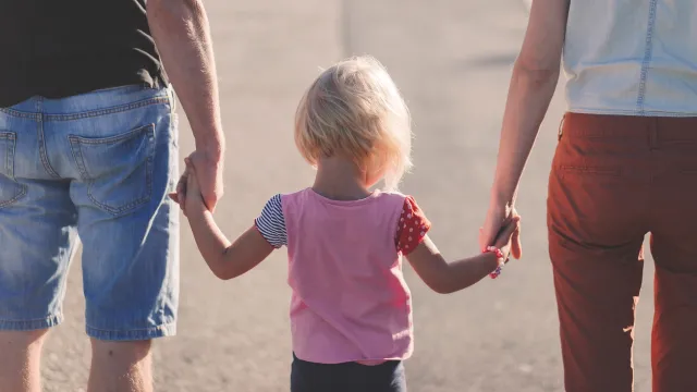 Stimmungsbild zum Beitrag: Von hinten wird ein Kind händehaltend zwischen ihren Eltern abgebildet.