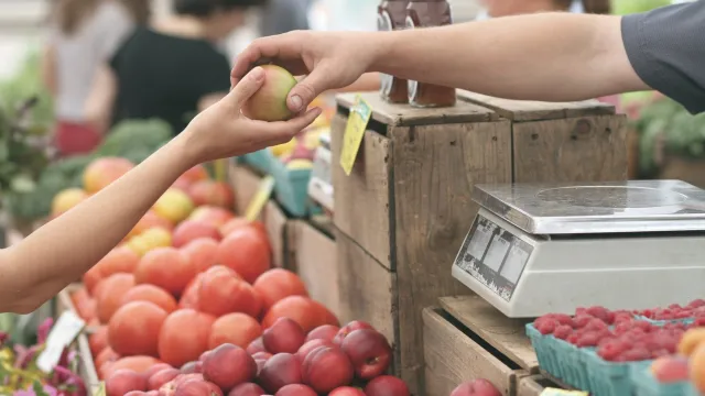 Stimmungsbild zum Beitrag: Der Verkauf eines Apfels an einem Obststand wird abgebildet.