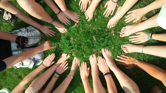 Stimmungsbild zum Beitrag: Es werden Hände und Füße, die im Kreis angeordnet sind auf einer Rasenfläche abgebildet.