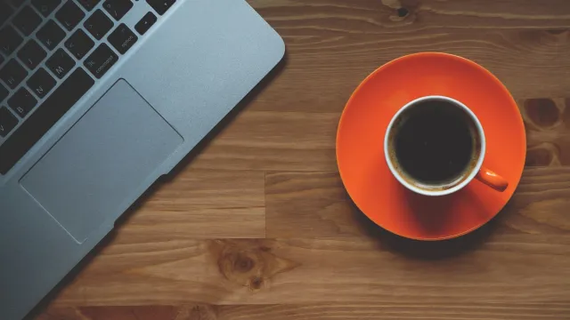 Stimmungsbild zum Beitrag: Es wird eine rote Kaffeetasse neben einem Laptop abgebildet.