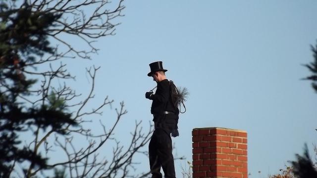 Ein Mann als Schornsteinfeger auf einem Dach