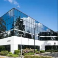 Bürogebäude mit großer Glassfassade, in der sich der Himmel spiegelt. Die Beete rund um das Gebäude sind mit Buchsbaum und weiteren Pflanzen angelegt.