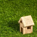 Stimmungsbild zum Beitrag: Ein kleines Modelhaus, das aus hölzernen Bauklötzen gebaut ist, wird abgebildet. Es steht auf einer Grasfläche.