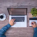 Stimmungsbild zum Beitrag: Es wird ein Laptop auf einem Schreibtisch aus der Vogelperspektive abgebildet.