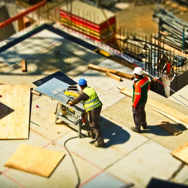 Zwei Männer auf einer Großbaustelle, die an einer Säge arbeiten