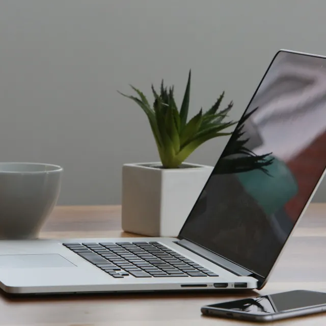 Stimmungsbild zum Beitrag: Es wird ein Laptop mit Handy, Blume und Becher abgebildet.