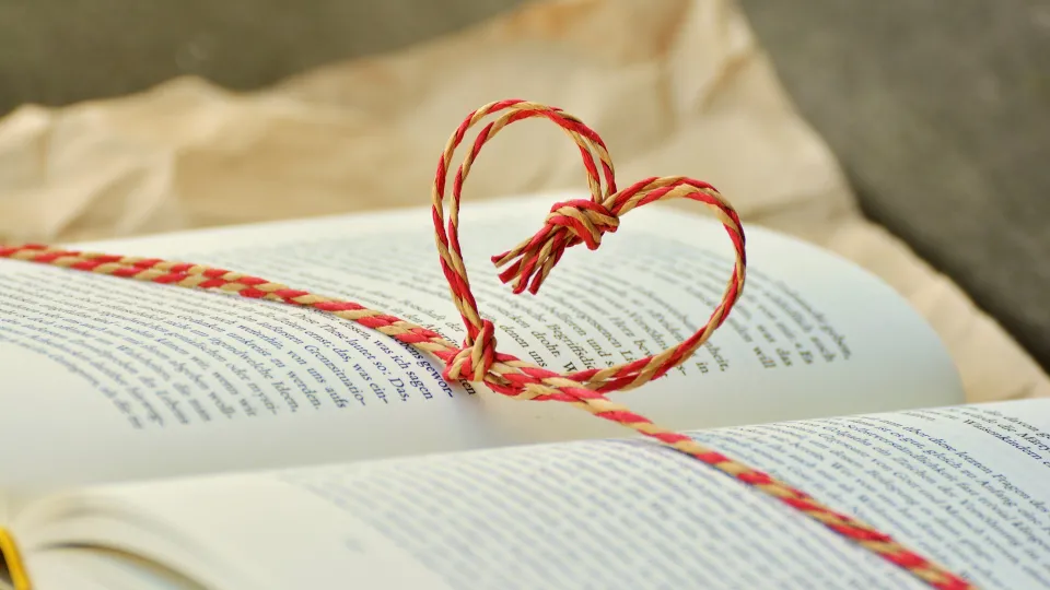 Stimmungsbild zum Beitrag: Ein aufgeschlagenes Buch, um das ein Band mit Herzform geknüpft ist, wird abgebildet.
