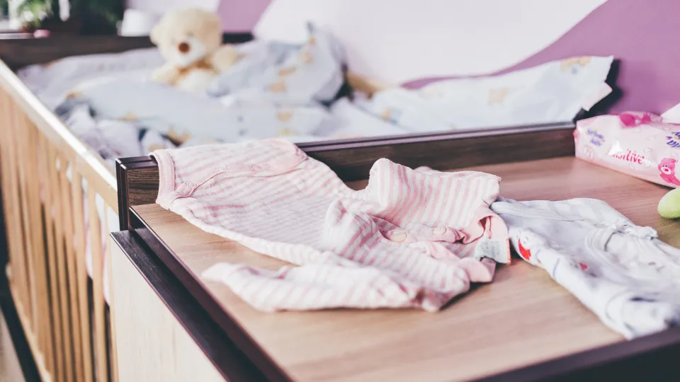 Stimmungsbild zum Beitrag: Es werden ein Babybett und eine Kommode mit Babykleidung abgebildet.