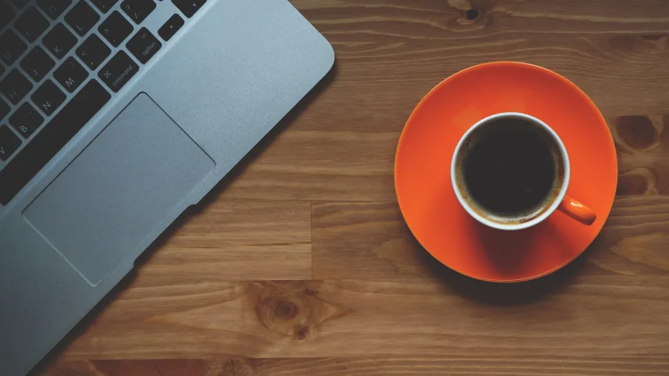 Stimmungsbild zum Beitrag: Es wird eine rote Kaffeetasse neben einem Laptop abgebildet.