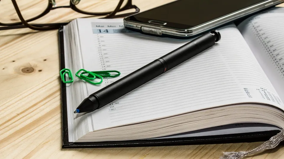 Stimmungsbild zum Beitrag: Es wird ein Notizblock mit Stift, Smartphone, Brille und Heftklammern abgebildet.
