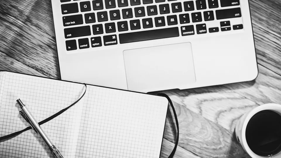 Stimmungsbild zum Beitrag: Es ist schwarz-weiß dargestellt und bildet einen Laptop mit Notizblock, Stift und gefüllten Kaffeebecher ab.