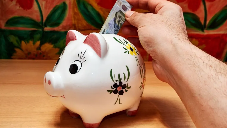 Stimmungsbild zum Beitrag: Es wird ein buntes Sparschwein gezeigt, in dem gerade eine Person 5 Euro einwirft.